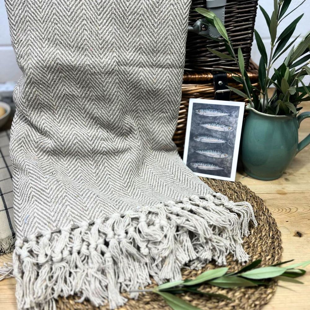 Textured throw blanket with tassels on a chair next to a plant and small chalkboard sign.