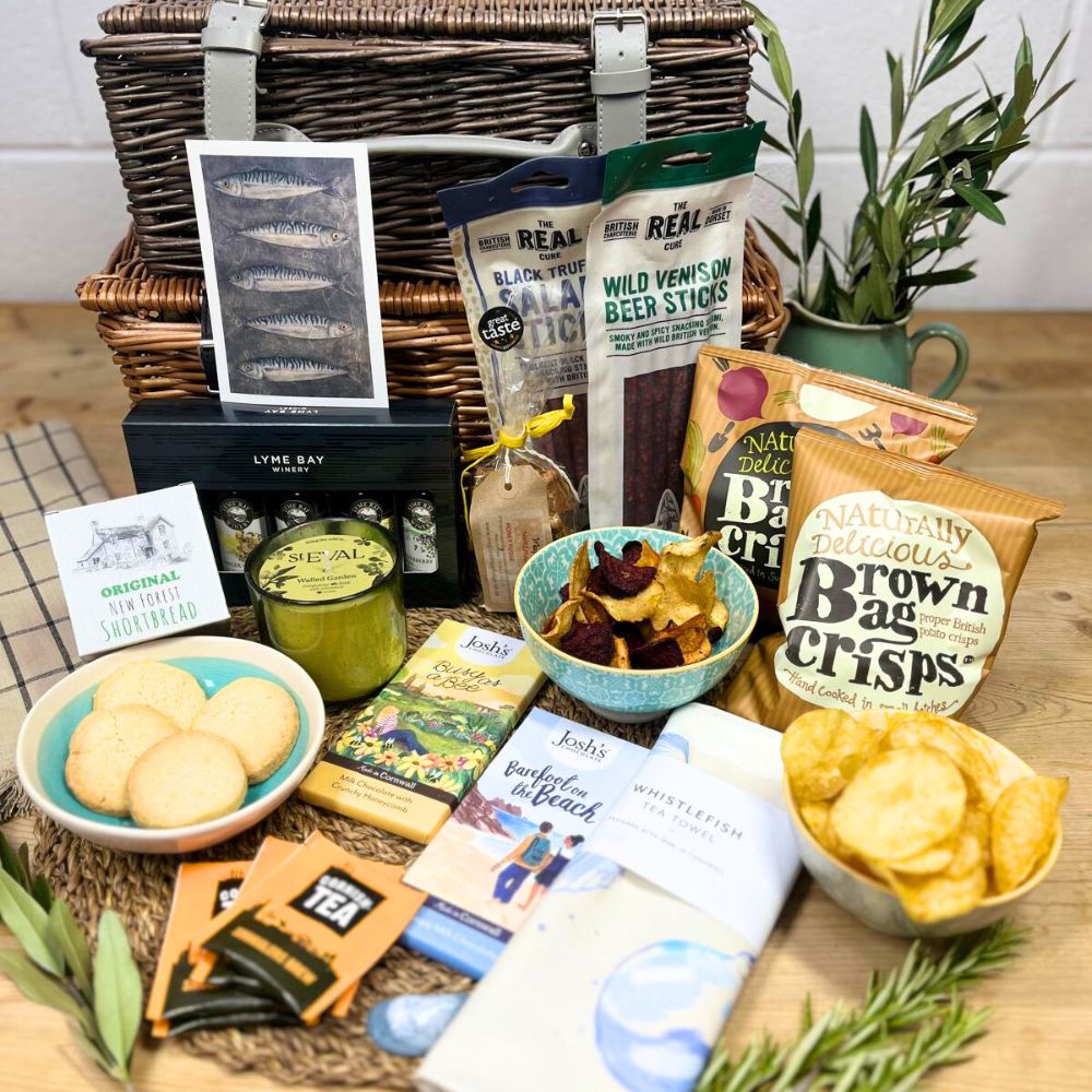Gourmet gift basket with snacks, tea, and other treats on a wooden table.