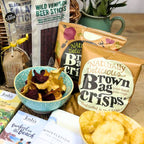 Assorted snack packages including 'Brown Bag Crisps' on a wooden surface.