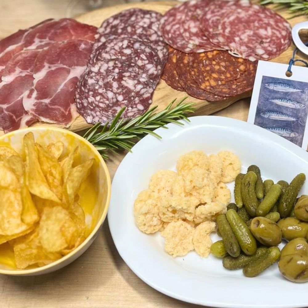 Assorted cured meats, chips, and pickles on a wooden board.