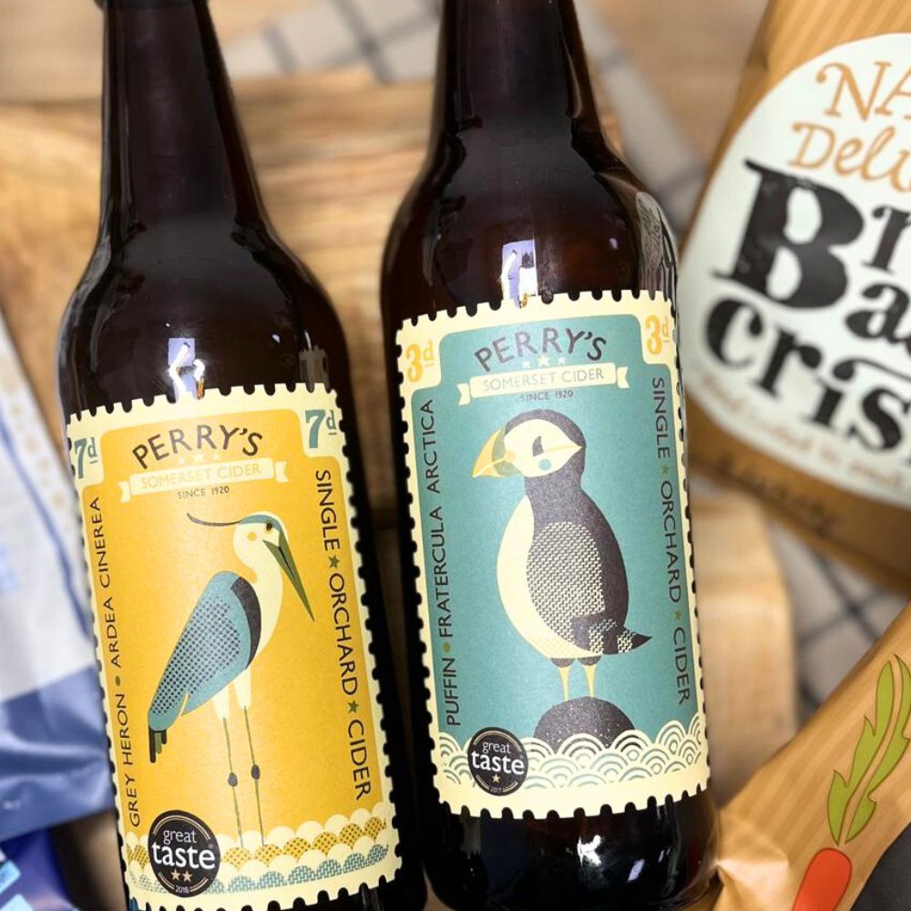 Two bottles of Perry's cider with bird illustrations on labels, placed on a wooden surface.