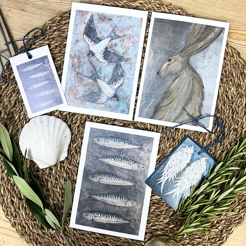 Three Sam Gabriel art prints arranged side by side with two small labels beneath them, decorated with scattered seashells and sprigs of greenery.