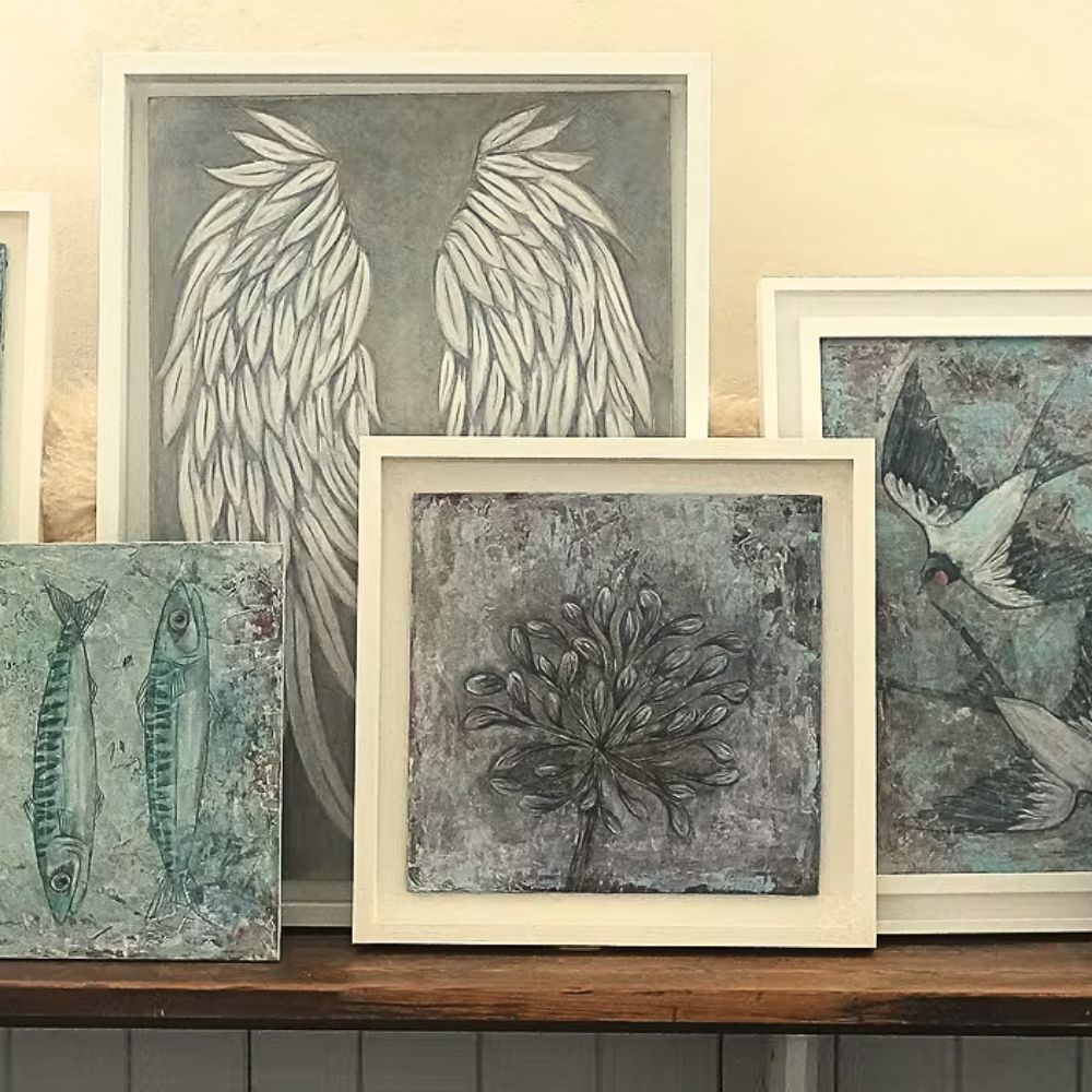 Framed artworks on a wooden shelf with a neutral background