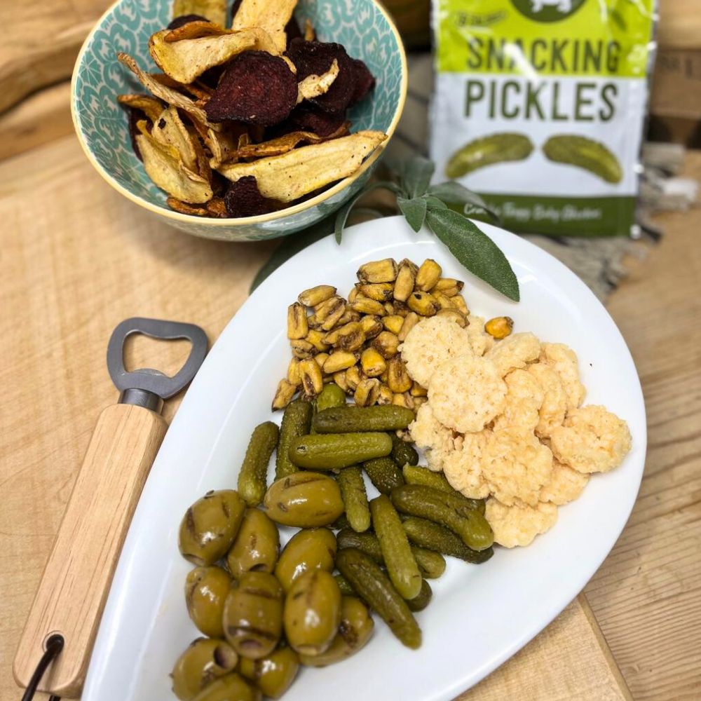 Assorted snacks including pickles, chips, and nuts on a plate with a bottle opener.