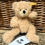 Beige teddy bear with a visible brand tag on a woven background
