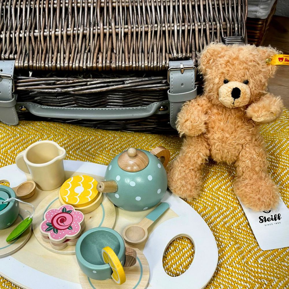 Teddy bear with a Steiff tag next to a toy tea set on a yellow textured surface.