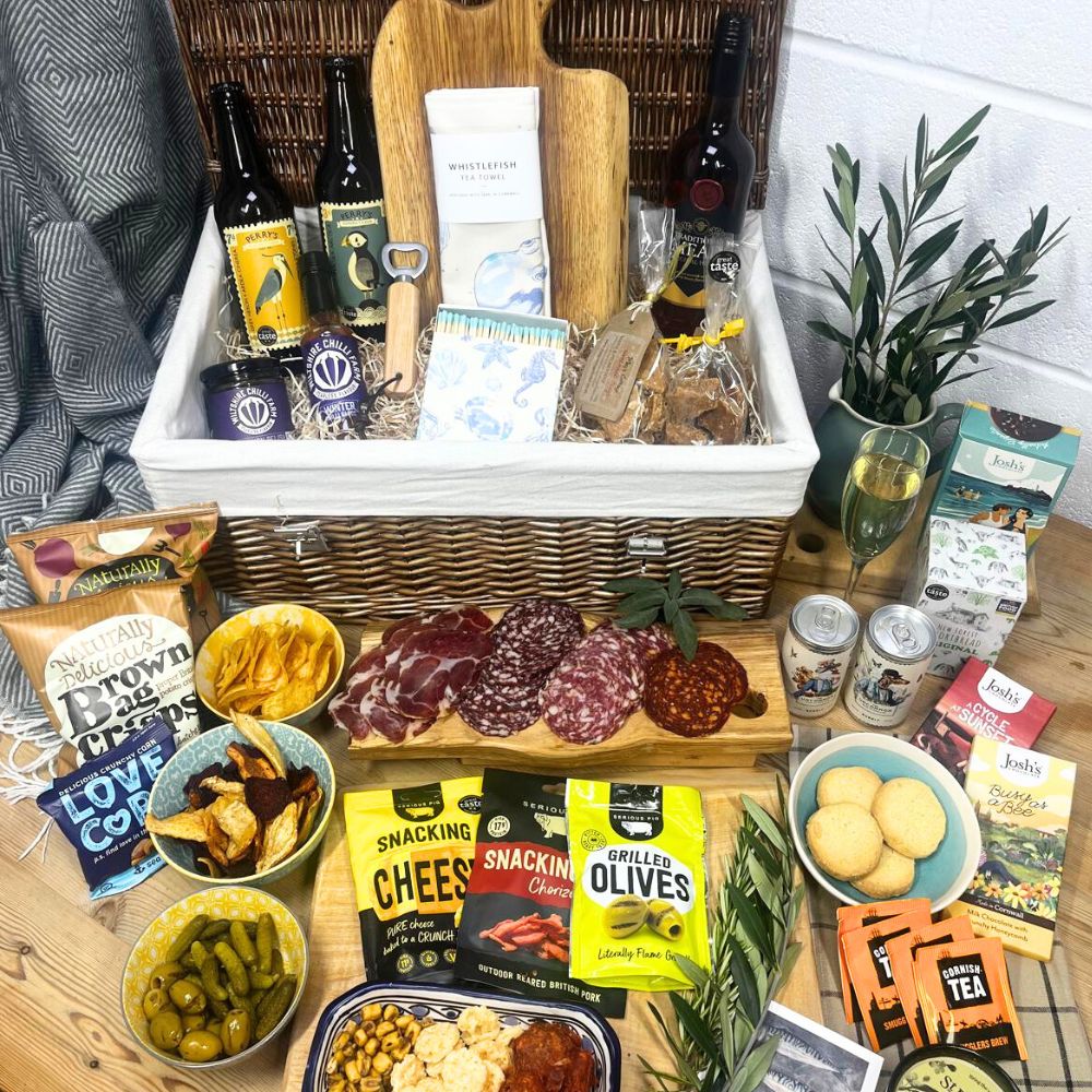 Gourmet gift basket with meats, cheeses, and snacks on a wooden table.