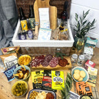 Gourmet gift basket with meats, cheeses, and snacks on a wooden table.