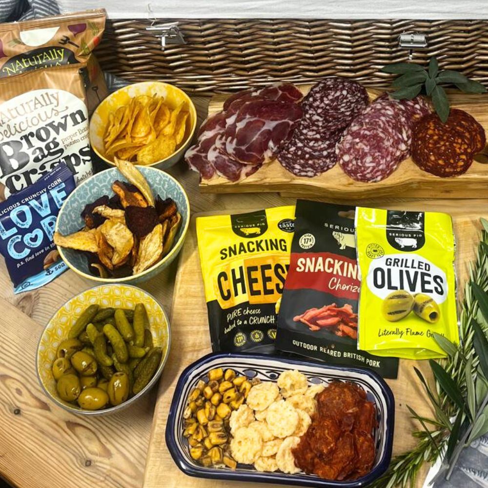 Assorted snacks including chips, olives, and charcuterie on a wooden board.