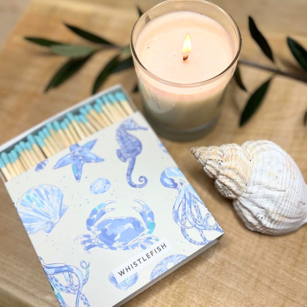 Candle, matches with sea-themed design, and shell on a wooden surface